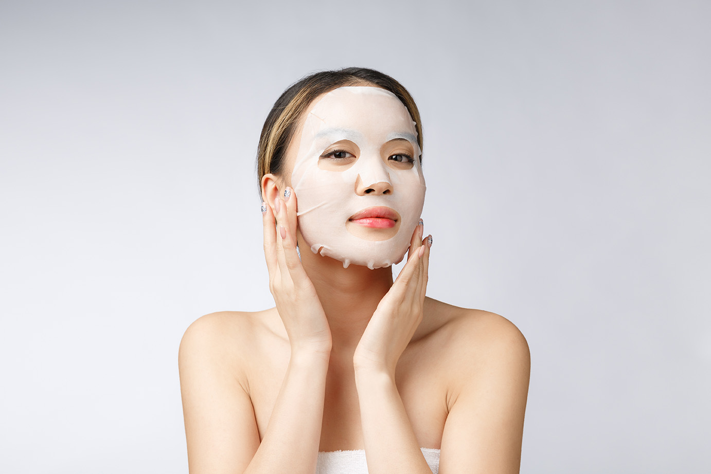 Beautiful asian woman applying paper sheet mask on her face white background