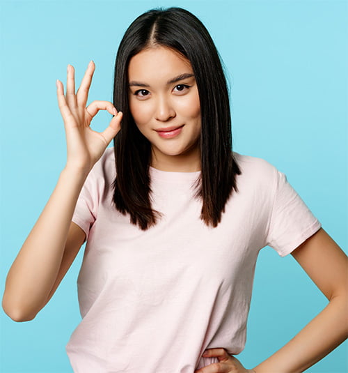 Smiling asian woman showing okay sign, gives approval, recommends smth good, standing over blue background